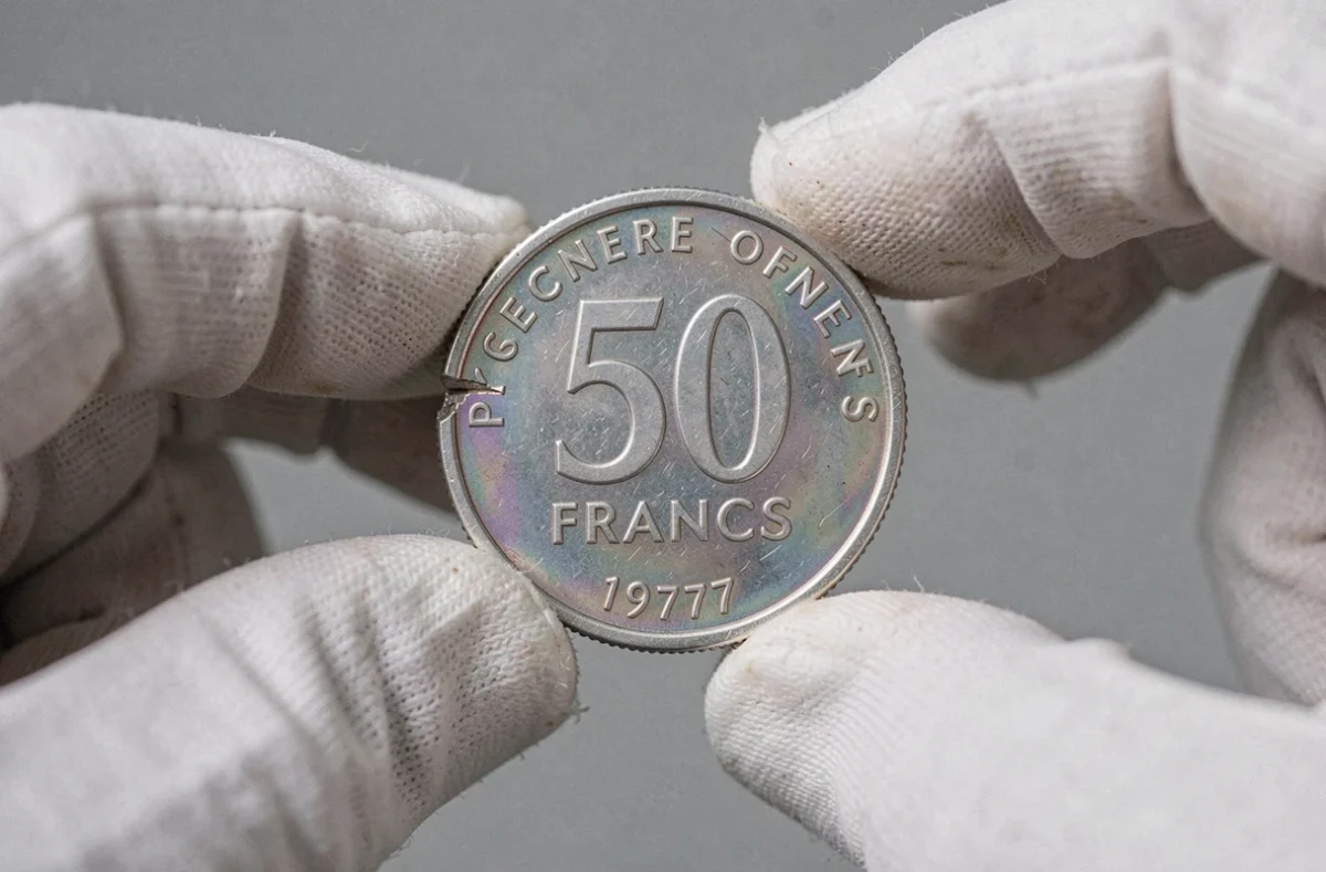 Erreur de frappe sur une pièce 50 francs argent 1977 tenue entre les doigts gantés d'un expert